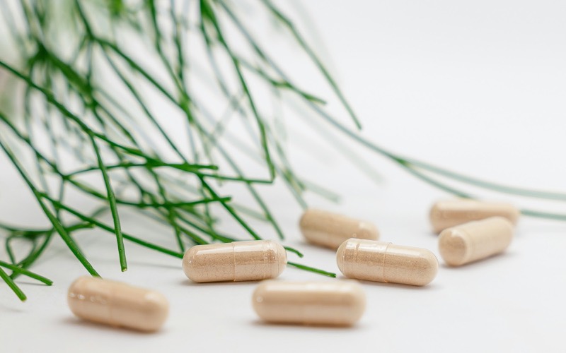 Unlabelled beige capsules on a white surface beside thin green stems