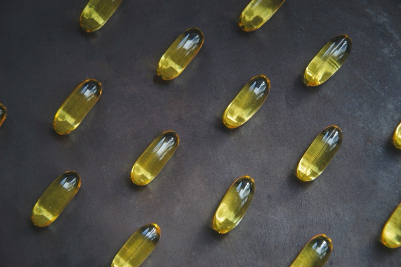 Rows of yellow oil softgels on a dark surface